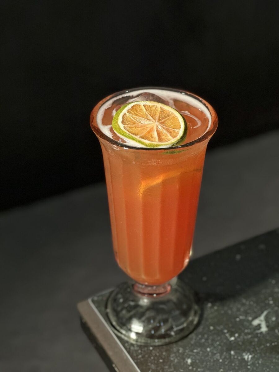 Pink-orange iced drink topped with a citrus wheel in a tall glass at EMC Kitchen