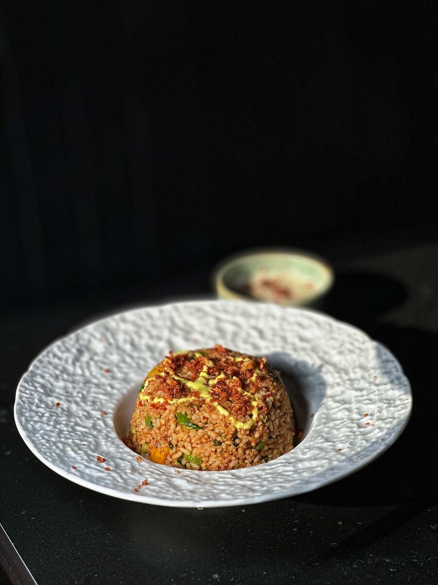 Mound of seasoned rice with a pale drizzle and browned topping on a white plate at EMC Kitchen