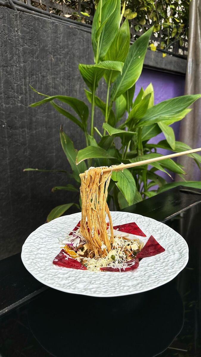 Thin noodles lifted with chopsticks above a white plate with shredded topping at EMC Kitchen